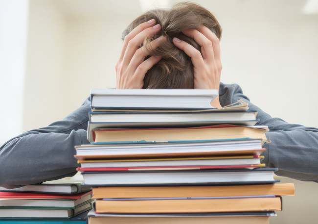 Copil stresat cu multe carti in fata lui