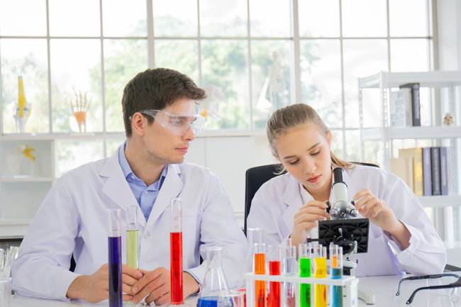 Barbat si femeie intr-un laborator de chimie testand cu eprubete